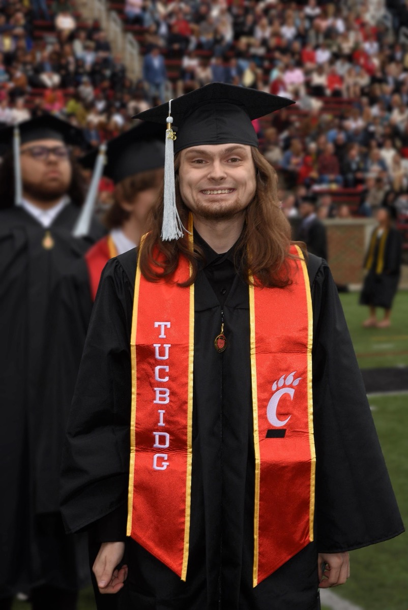Levi Huff smiling in University of Cincinnati cap and gown at graduation ceremony with crowd in background