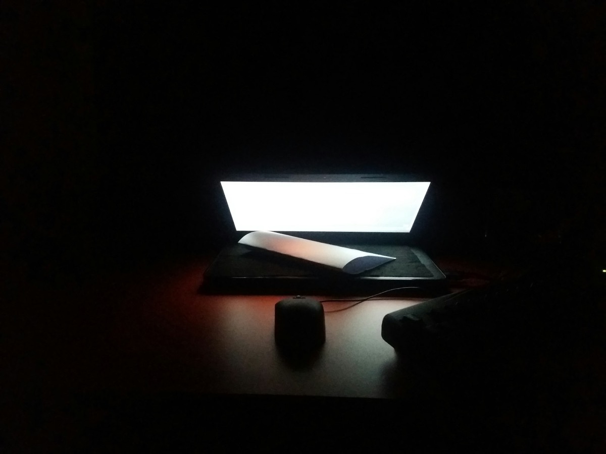 An open laptop on a wooden desk, lit warm in an otherwise dark room